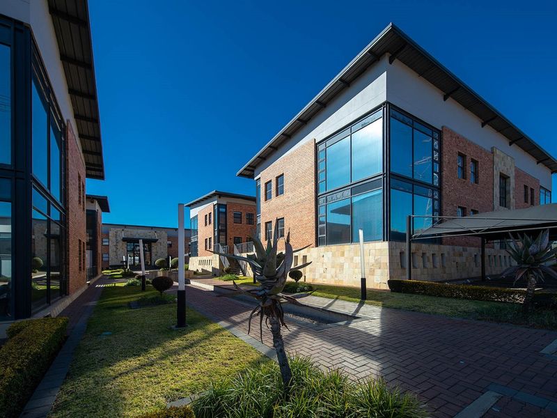 Modern commercial office complex featuring brick and stone facades, large glass windows, paved walkways, and landscaped grounds with integrated carports.
