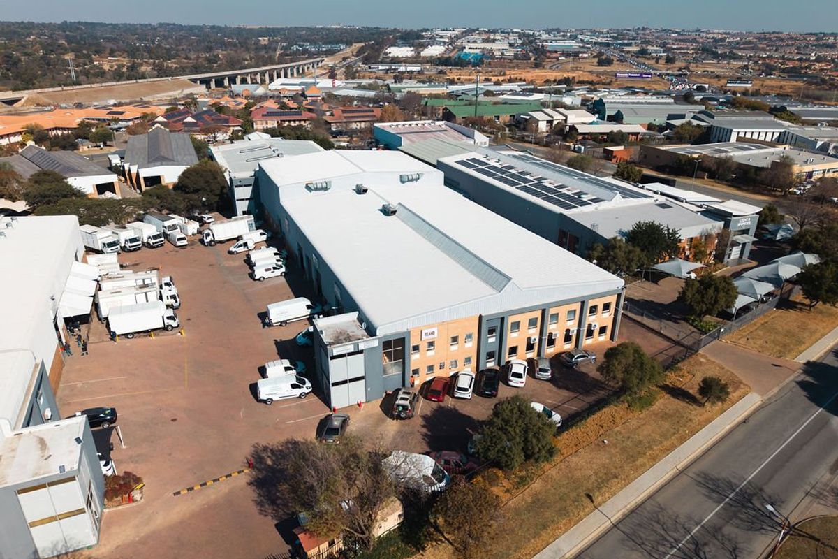Aerial view of an industrial property featuring a large warehouse facility, extensive asphalt yard space, and perimeter security fencing.