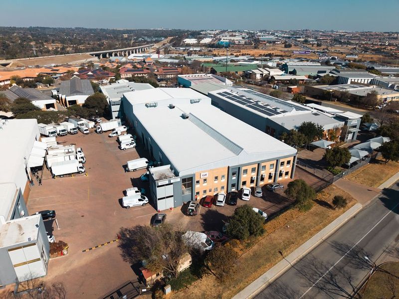 Aerial view of an industrial property featuring a large warehouse facility, extensive asphalt yard space, and perimeter security fencing.