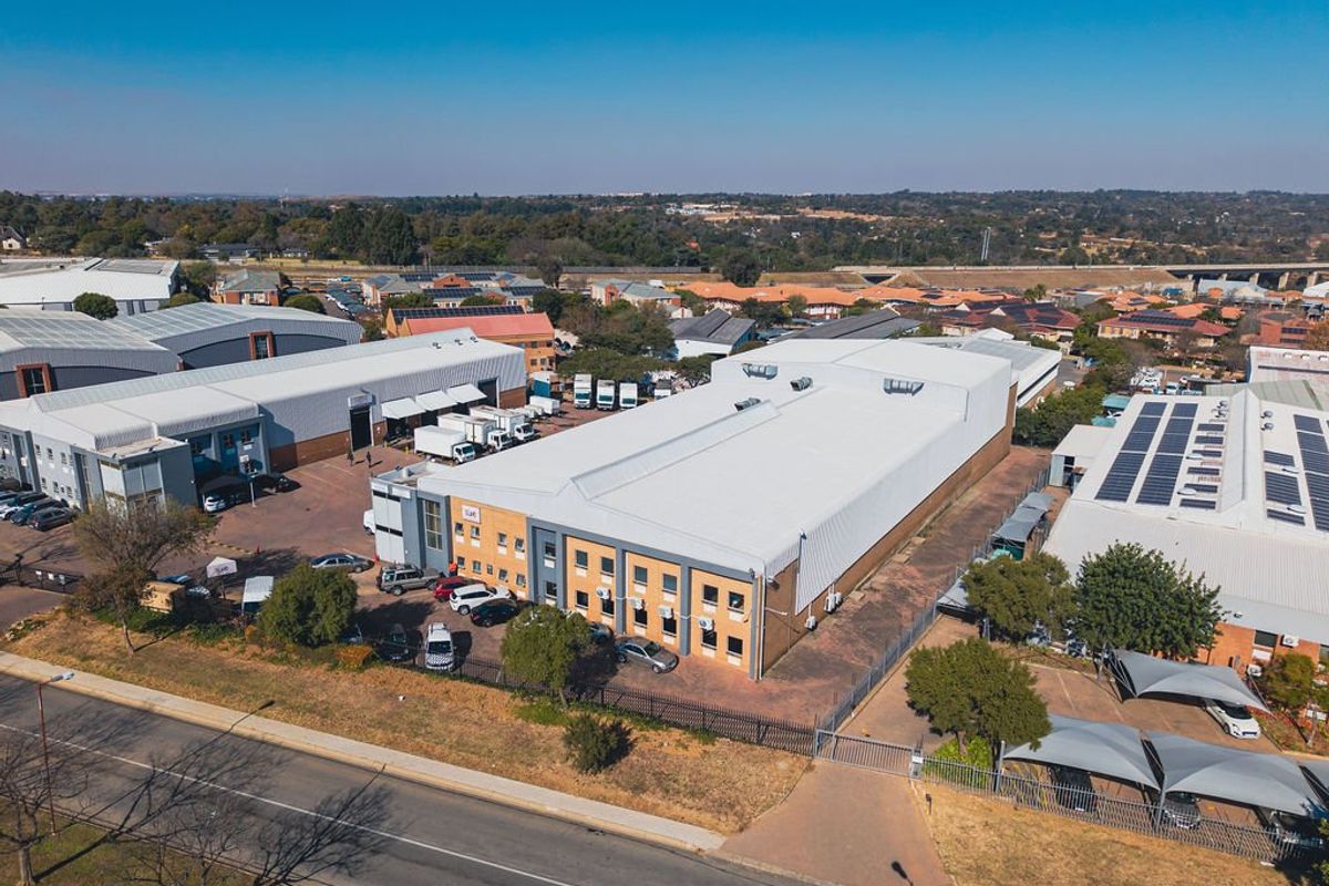 Aerial view of an industrial property complex featuring large warehouse structures, paved parking areas, and secure perimeter fencing in a commercial estate setting.