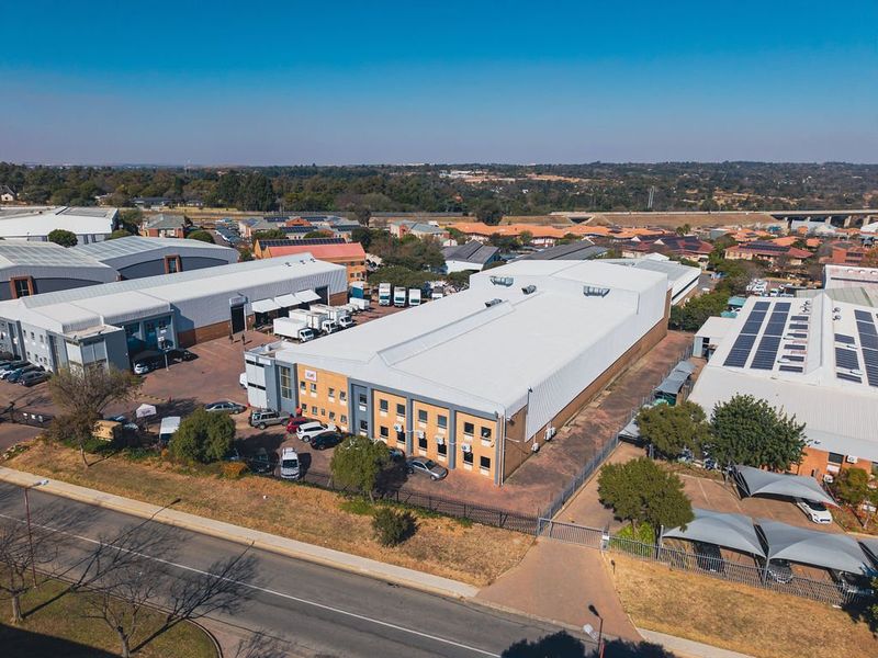 Aerial view of an industrial property complex featuring large warehouse structures, paved parking areas, and secure perimeter fencing in a commercial estate setting.