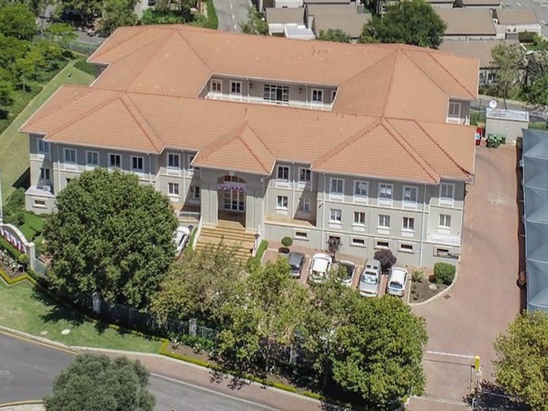 Aerial view of a commercial office building featuring a central courtyard, terracotta roof, paved parking area, and landscaped grounds.