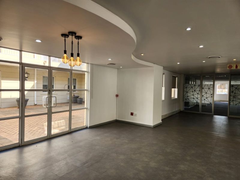 Spacious open-plan commercial area featuring modern recessed lighting, large glass doors leading to an outdoor courtyard, and neutral tiled flooring.