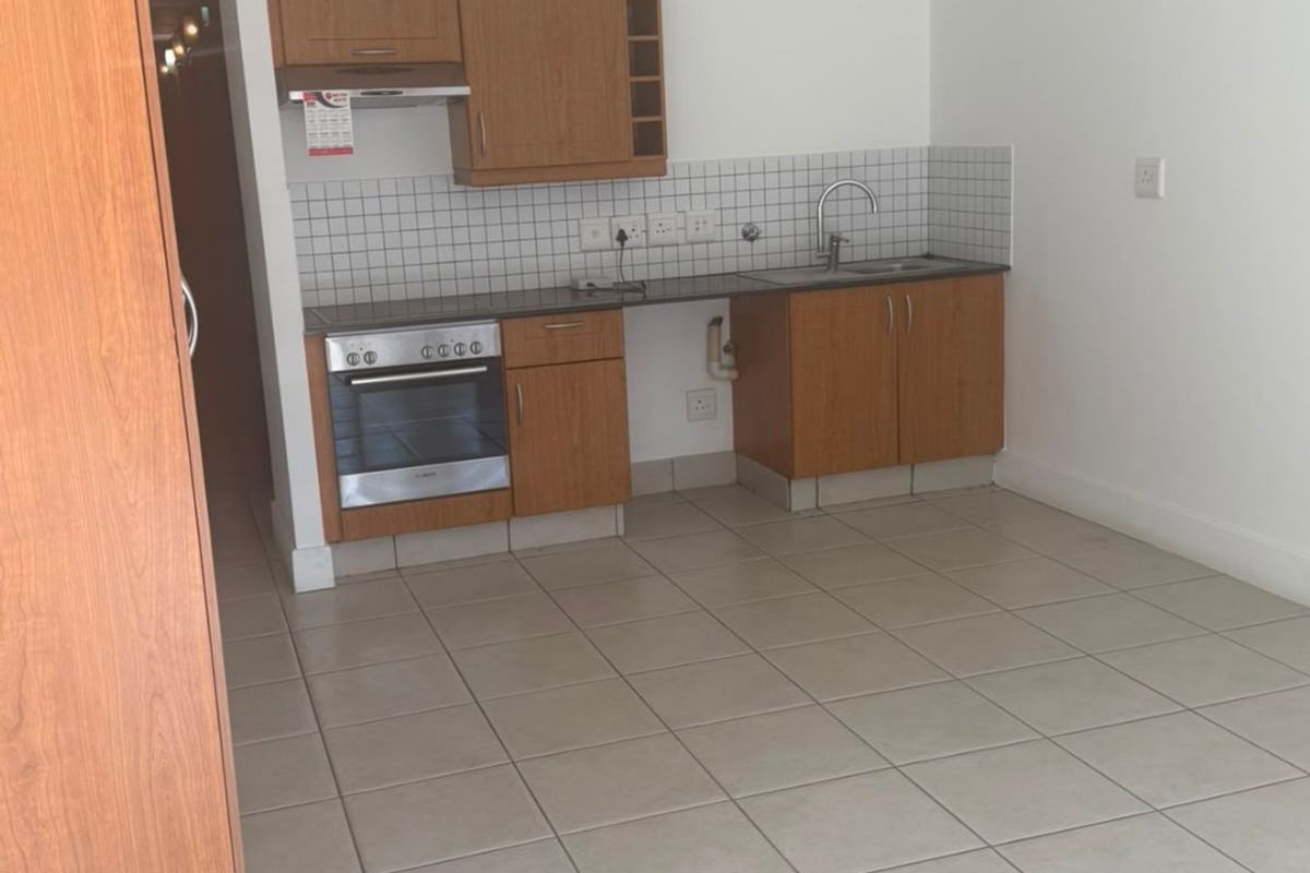 A compact, empty kitchen featuring wooden cabinetry, a built-in oven, extractor fan, and tiled flooring with a neutral backsplash.