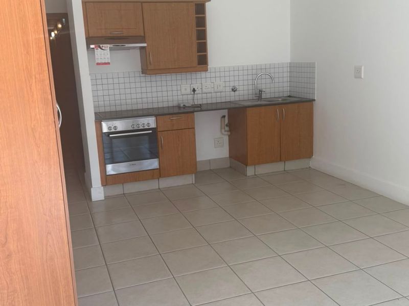 A compact, empty kitchen featuring wooden cabinetry, a built-in oven, extractor fan, and tiled flooring with a neutral backsplash.