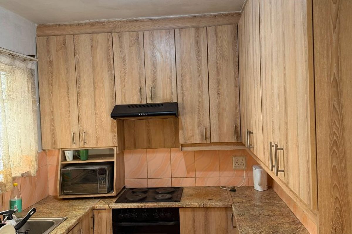 A functional kitchen featuring wood-look laminate cabinetry, granite countertops, a built-in oven with hob, and a tiled backsplash.