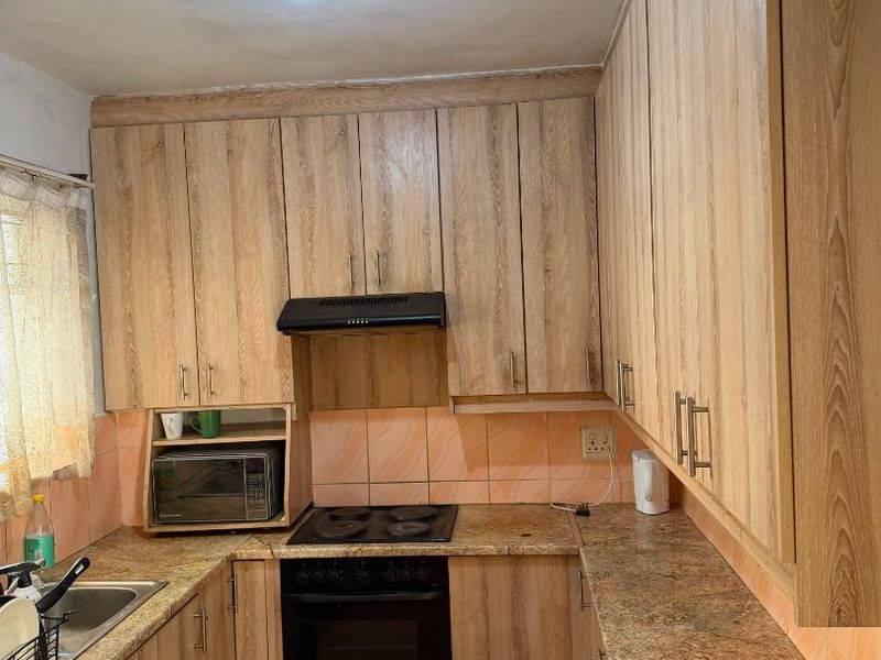 A functional kitchen featuring wood-look laminate cabinetry, granite countertops, a built-in oven with hob, and a tiled backsplash.