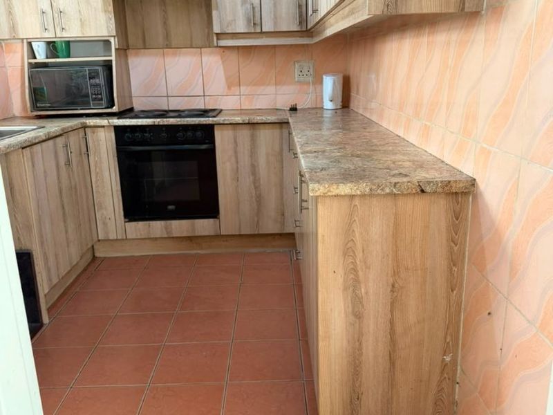 A functional kitchen featuring wood-look cabinetry, stone-effect countertops, built-in oven, hob, and extractor fan, finished with ceramic wall and floor tiles.