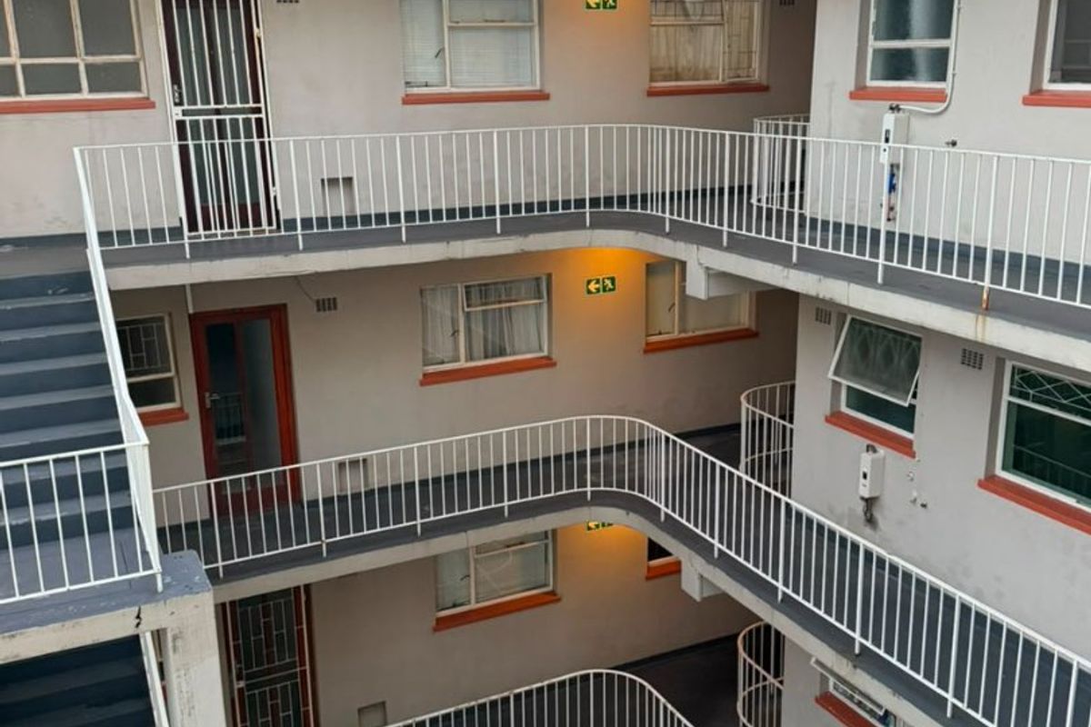 Exterior view of a multi-story apartment building featuring open-air walkways, metal safety railings, and external staircases.