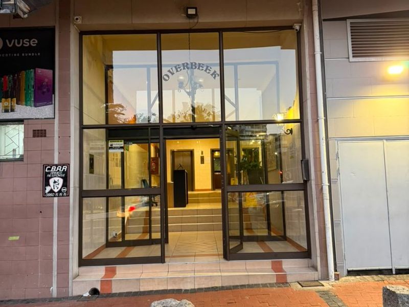 Main entrance to the Overbeek apartment building featuring a glass door facade and tiled steps leading into the lobby area.