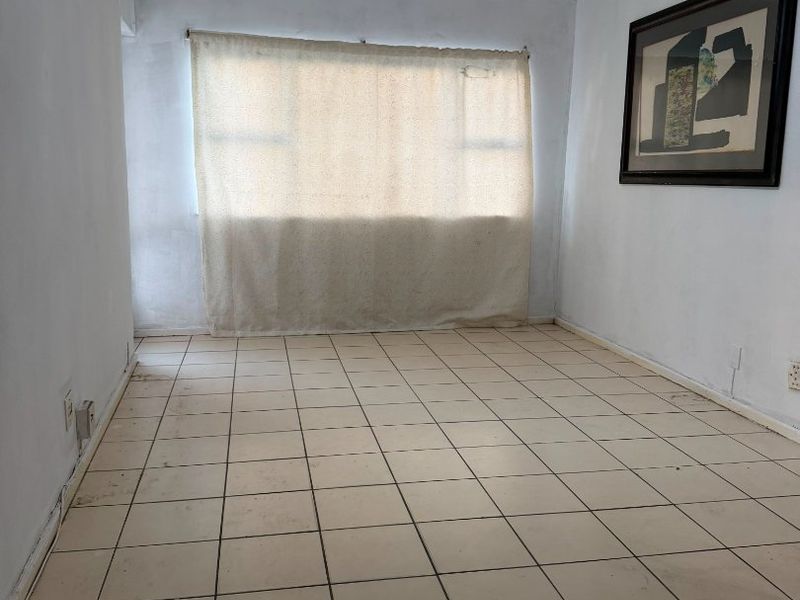 An empty living room featuring ceramic floor tiles, a ceiling fan, and neutral walls, offering a blank canvas for renovation or interior design.