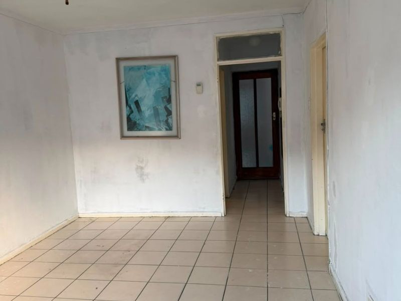 An empty living area featuring ceramic floor tiles, a ceiling fan, and access to an internal hallway.