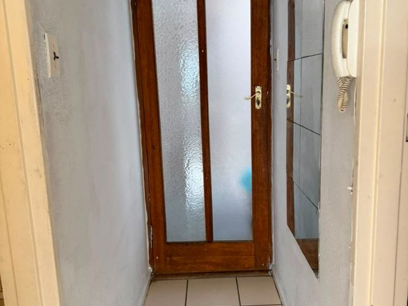 A narrow hallway featuring tiled flooring, a timber-framed glass door, and a wall-mounted intercom system.