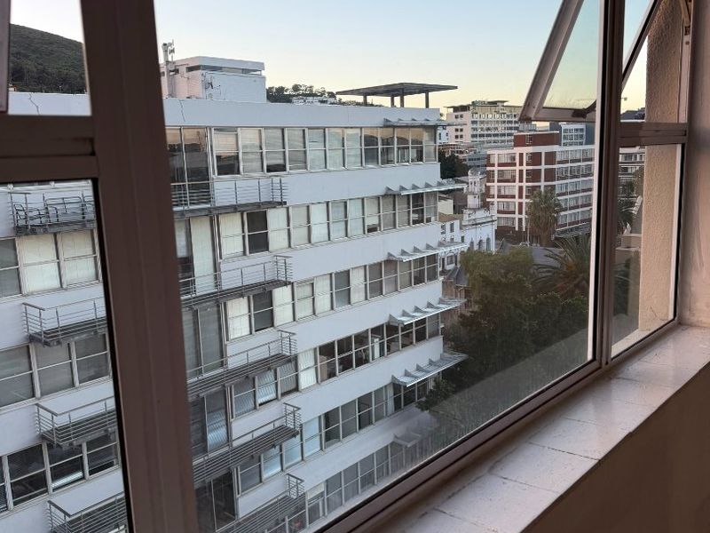 An elevated urban view looking out from an apartment window towards surrounding city buildings.