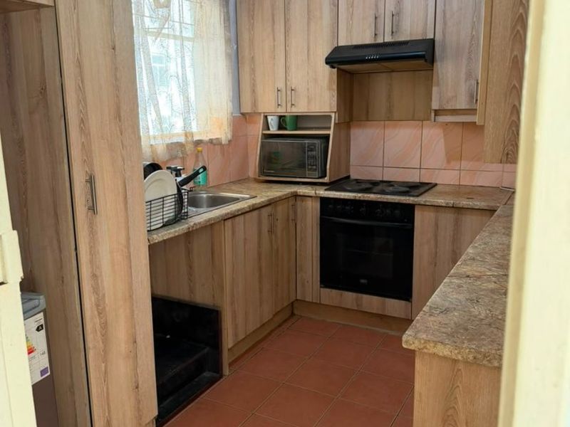 A functional kitchen featuring wood-look cabinetry, stone-effect countertops, built-in oven, electric hob, and extractor fan with tiled flooring and backsplash.