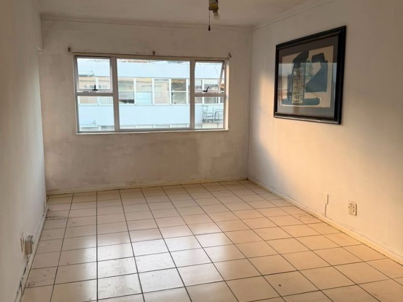 An empty bedroom featuring tiled flooring, a ceiling fan, and large windows, offering a blank canvas for renovation or interior design updates.