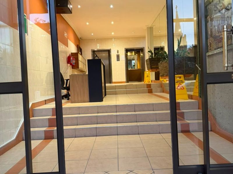 Building entrance lobby featuring tiled flooring, glass sliding doors, reception area, and elevator access.