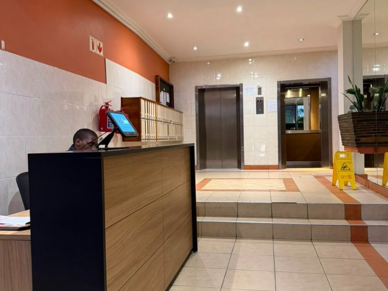 Apartment building lobby featuring a reception desk, tiled flooring, and elevator access.