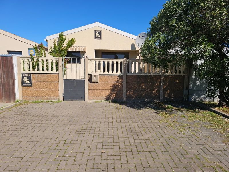 Front view of the property featuring a paved driveway, secure boundary wall with balustrade, and pedestrian gate access.