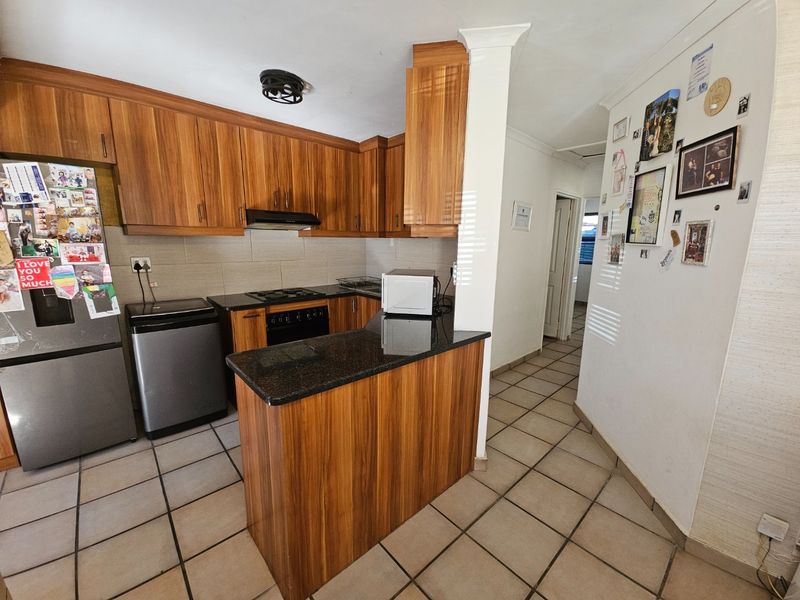 A functional kitchen featuring wood-finish cabinetry, granite countertops, a built-in oven with gas hob, and tiled flooring.