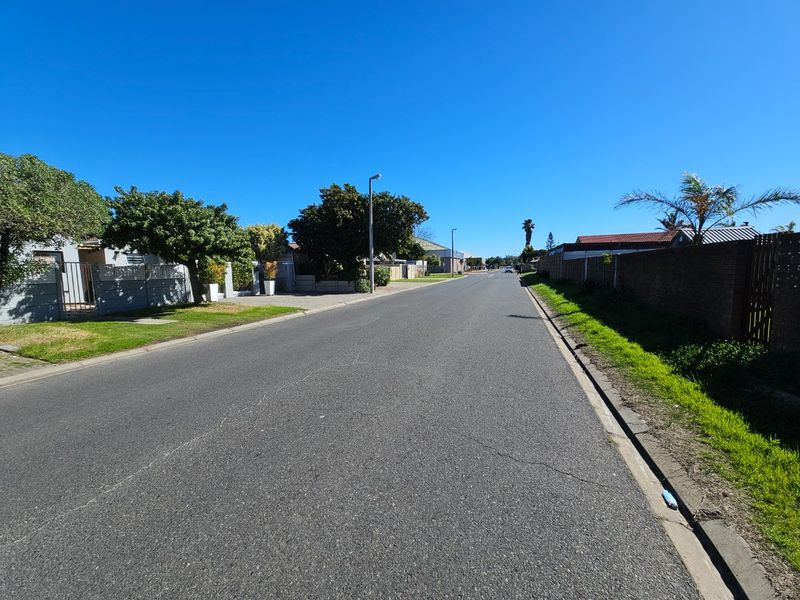 A clear street view showing the residential road, surrounding boundary walls, and established trees in the neighbourhood.