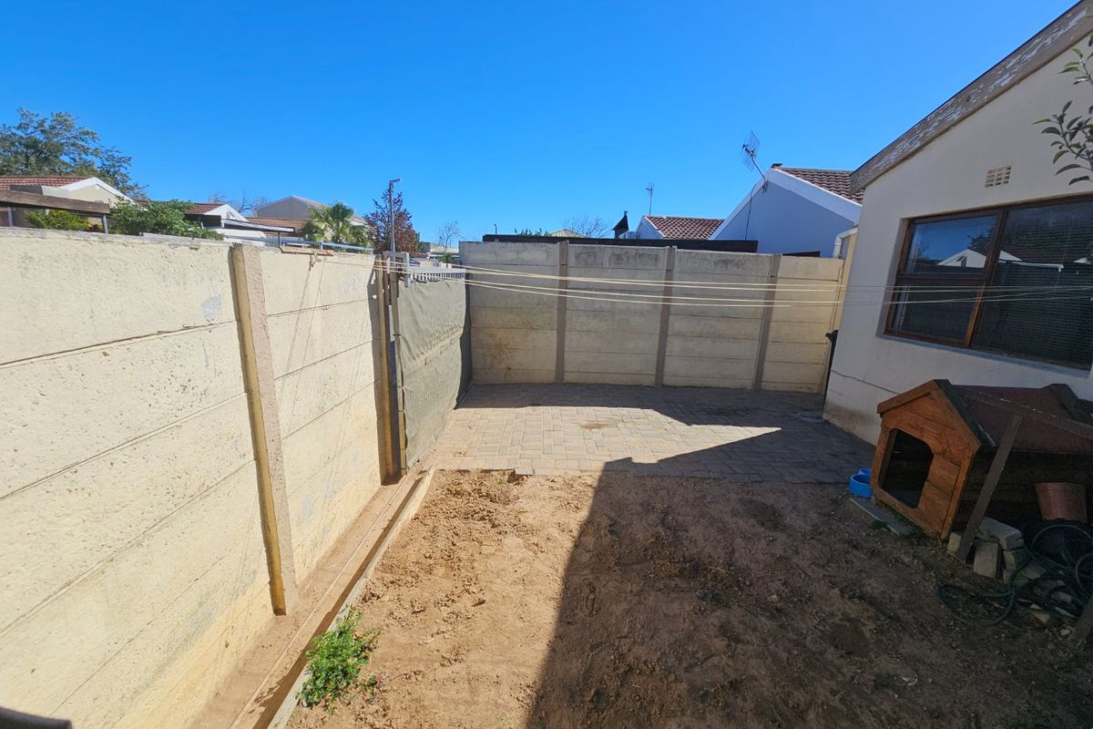 Rear courtyard featuring a paved patio area, precast concrete boundary walls, and an unlandscaped garden section requiring attention.