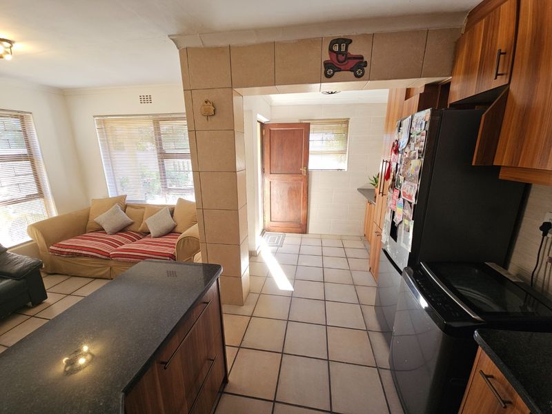 Open-plan living and kitchen area featuring tiled flooring, built-in cabinetry with stone countertops, and direct access to the exterior via a timber door.