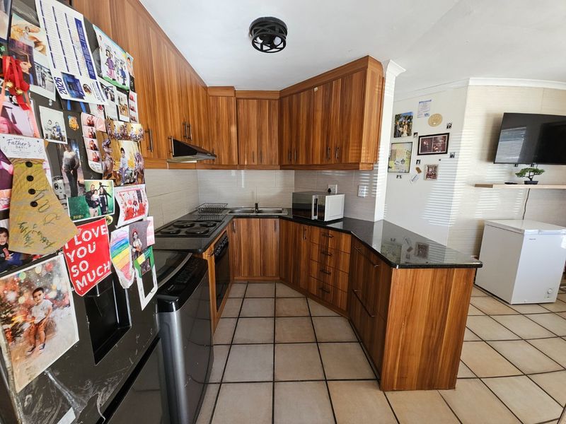 A functional kitchen featuring wood-grain cabinetry, granite countertops, built-in oven, electric hob, and tiled flooring, offering a practical layout for daily meal preparation.