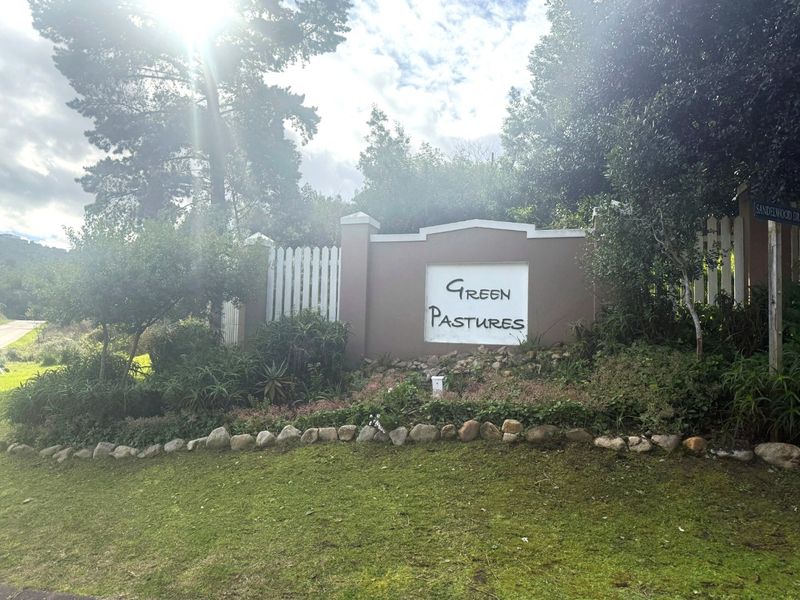 Entrance signage and boundary wall for Green Pastures, featuring a well-maintained garden, stone edging, and white picket fencing.