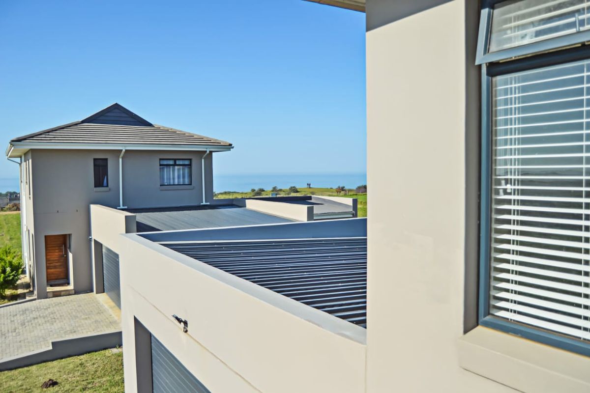 An elevated view of the property exterior featuring modern roof lines, aluminium window frames, and a paved driveway with a distant ocean view.