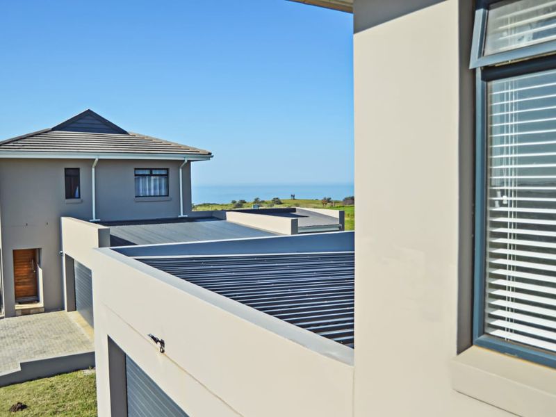 An elevated view of the property exterior featuring modern roof lines, aluminium window frames, and a paved driveway with a distant ocean view.