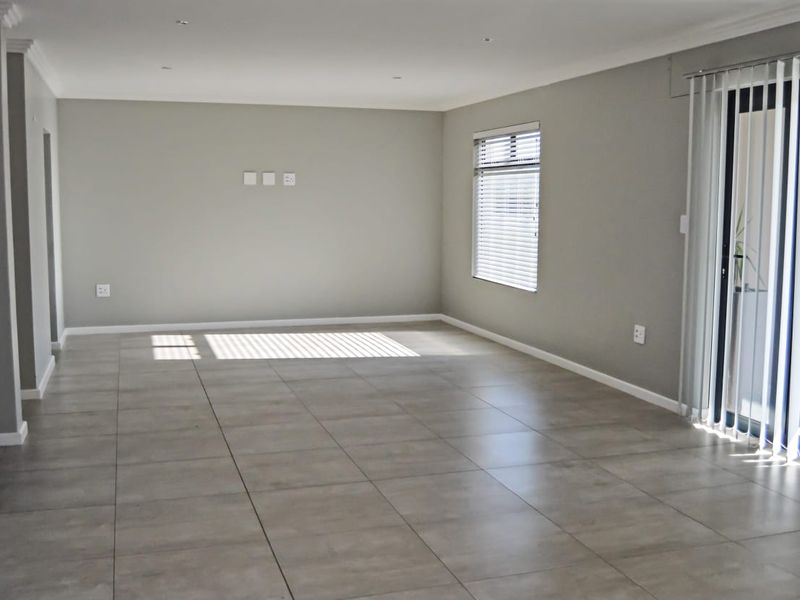 A spacious, neutral-toned living area featuring large format floor tiles, recessed lighting, and direct access to an outdoor space via a sliding glass door.