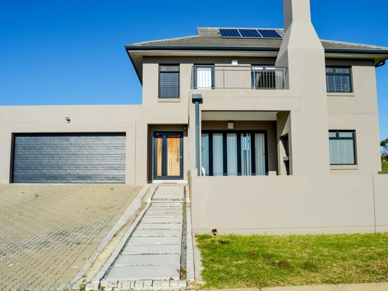 Modern double-story residential home featuring a double garage, solar panels, a balcony, and a paved driveway with a concrete entrance walkway.