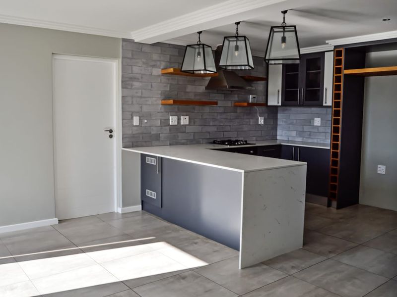 Modern kitchen featuring stone countertops, dark cabinetry, gas hob, extractor fan, and stylish pendant lighting with neutral tiled flooring.
