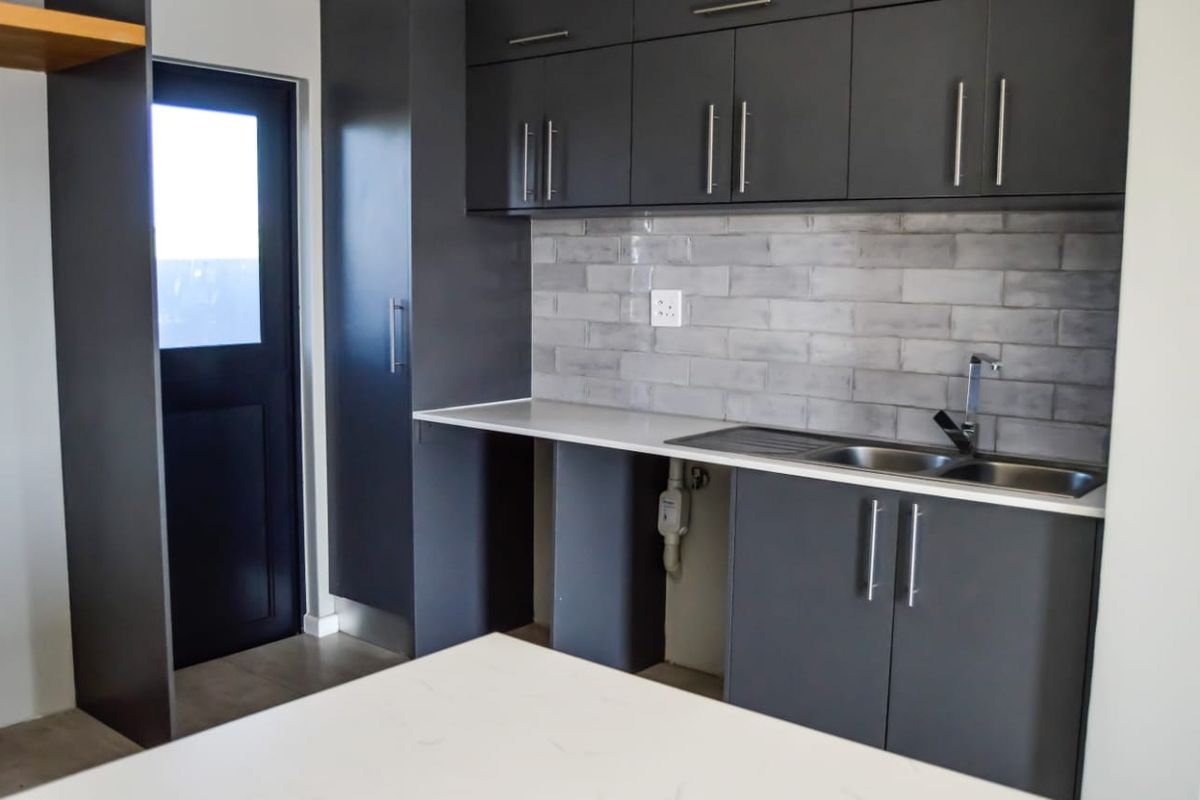 Modern kitchen featuring charcoal cabinetry, subway tile backsplash, stone countertops, and a stainless steel sink with direct access to an exterior door.