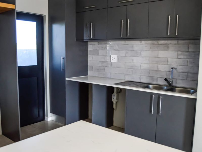 Modern kitchen featuring charcoal cabinetry, subway tile backsplash, stone countertops, and a stainless steel sink with direct access to an exterior door.