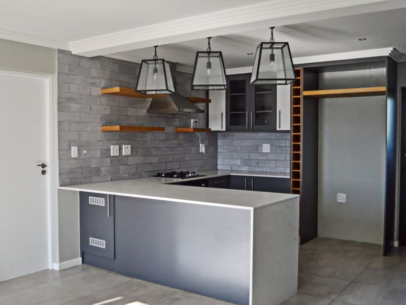Modern kitchen featuring dark cabinetry, stone countertops, a gas hob with extractor, floating shelves, and stylish pendant lighting in an open-plan layout.