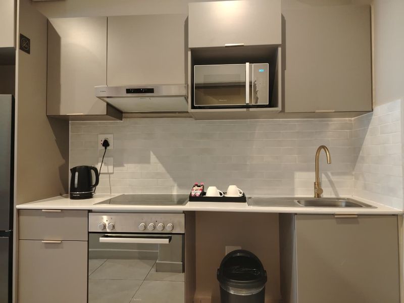 Modern kitchen featuring sleek grey cabinetry, stone countertops, subway tile backsplash, integrated appliances, and a stylish brass faucet.