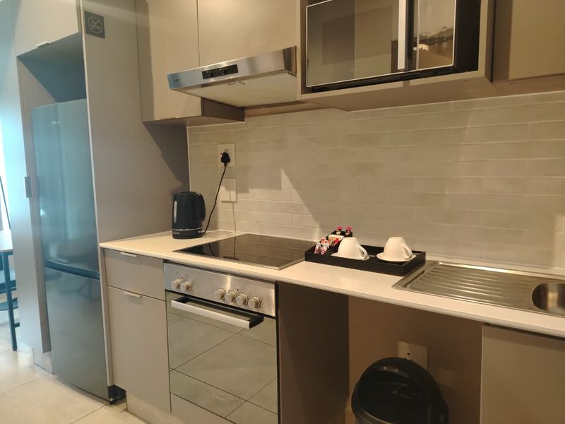 Modern kitchen featuring sleek cabinetry, stone countertops, integrated oven, hob, extractor fan, and built-in microwave with a clean tiled backsplash.