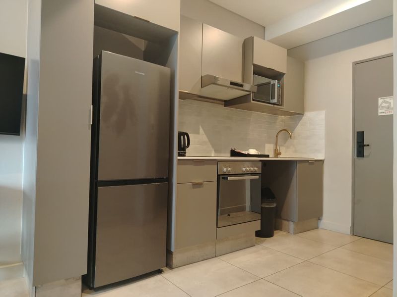 A modern, compact kitchen featuring sleek grey cabinetry, stainless steel appliances, a tiled backsplash, and contemporary fixtures.