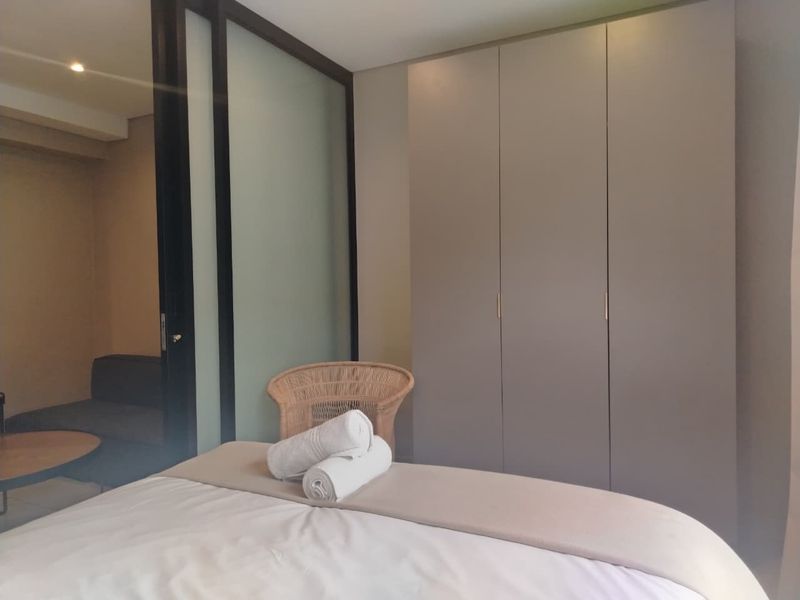 A modern bedroom featuring a large built-in wardrobe and a sleek sliding glass partition separating the sleeping area from the adjacent space.