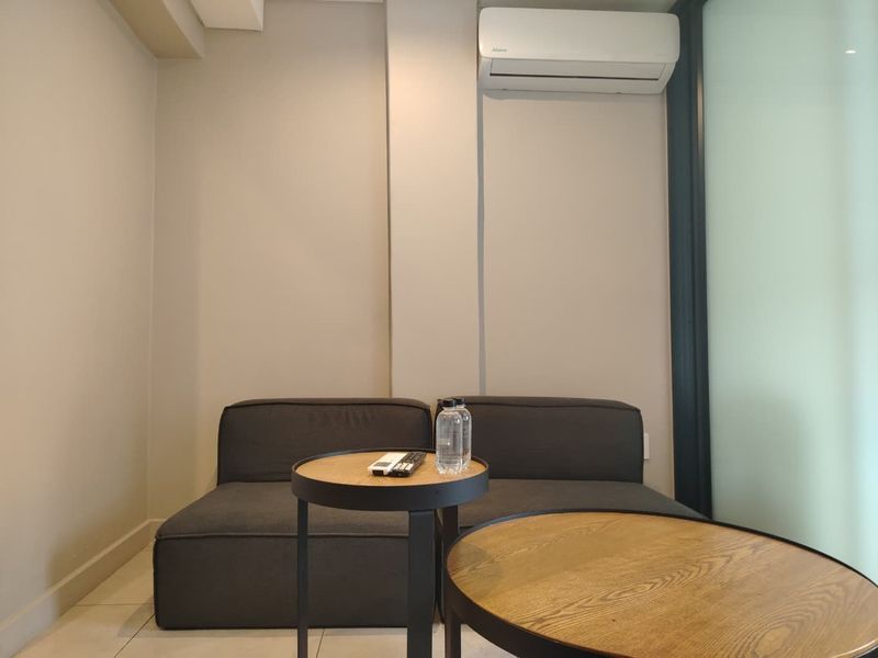 A compact living area featuring neutral walls, tiled flooring, and a wall-mounted split-system air conditioner.