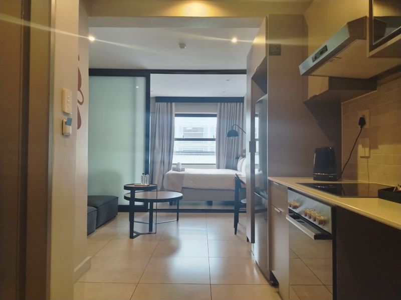 Open-plan apartment layout featuring a modern kitchen with built-in appliances, tiled flooring, and a sliding partition leading to the bedroom area.