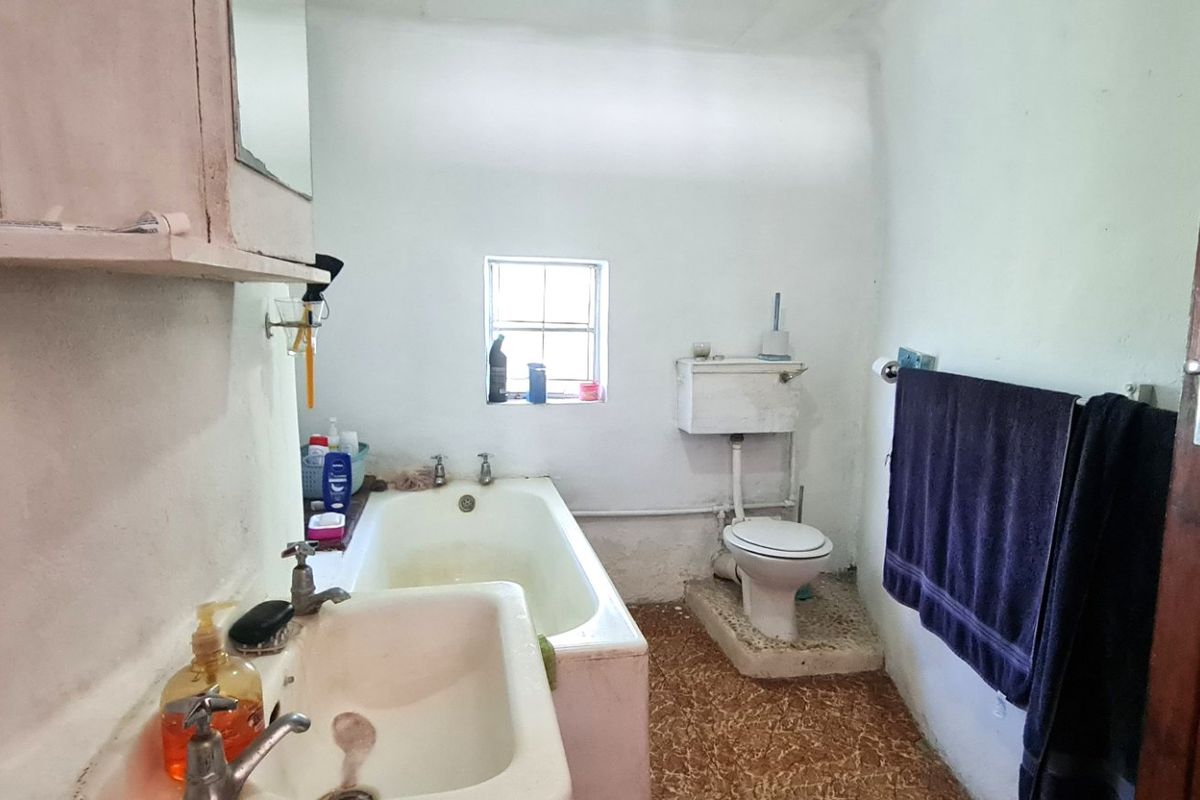 A dated bathroom featuring a pedestal sink, bathtub, and high-level cistern toilet, requiring modernization of finishes and fixtures.