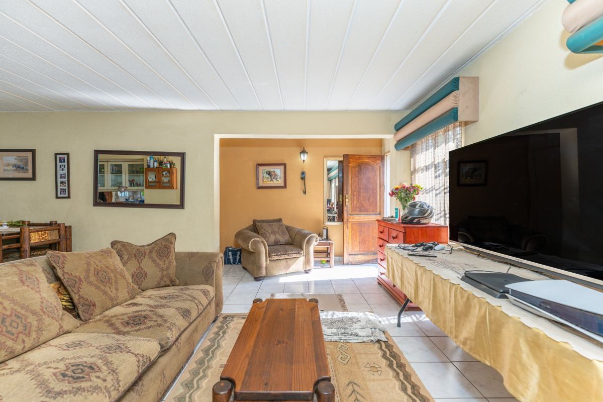 A living room area featuring tiled flooring and a timber entrance door, offering a functional space with potential for modern updates.