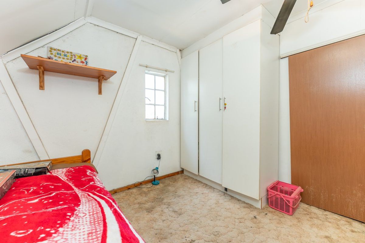 A bedroom featuring a sloped ceiling, built-in wardrobe, and timber shelving, requiring cosmetic updates to the flooring and wall finishes.