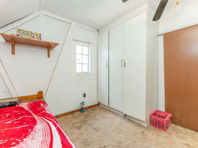 A bedroom featuring a sloped ceiling, built-in wardrobe, and timber shelving, requiring cosmetic updates to the flooring and wall finishes.