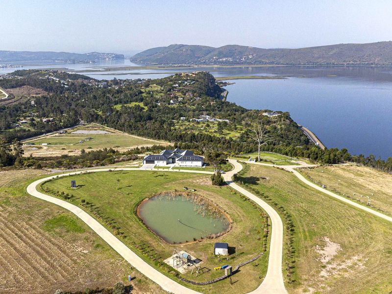 Aerial view of a residential property featuring a large plot of land, a private pond, paved driveway, and a house equipped with solar panels.