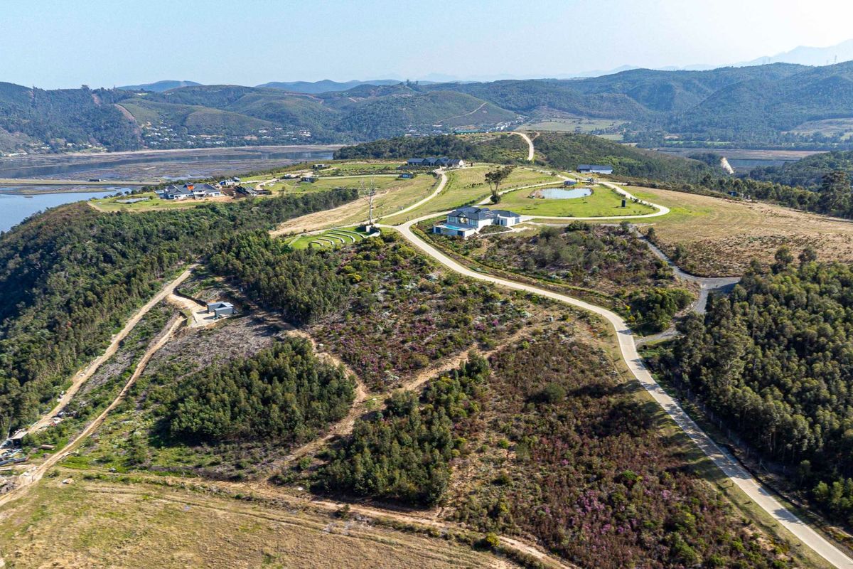 An aerial view of a residential estate featuring paved access roads, natural landscape, and proximity to a water body.