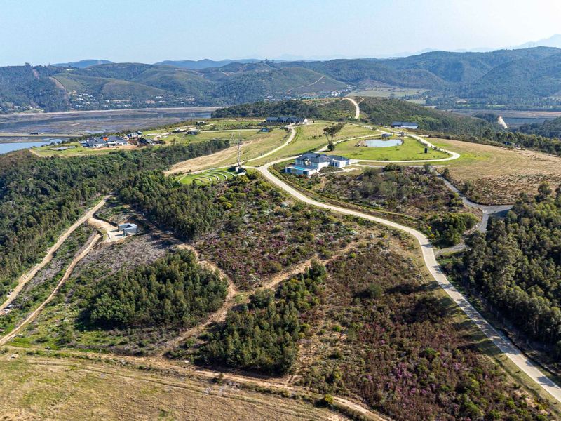 An aerial view of a residential estate featuring paved access roads, natural landscape, and proximity to a water body.